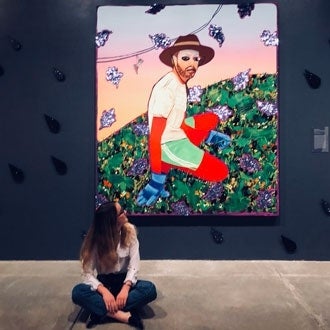 A young woman sits and smiles at a painting 